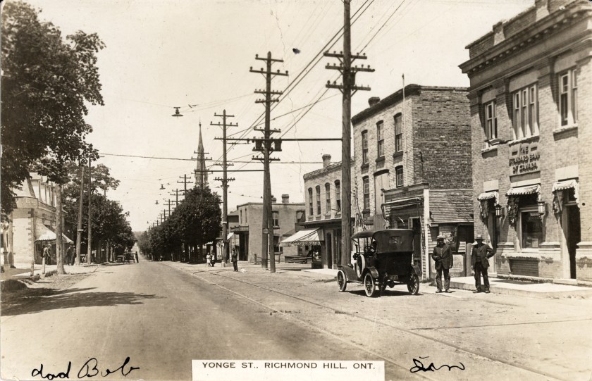 An old black and white photograph looking north on Yonge Street near the corner of Arnold Crescent featuring an old car with two men standing beside it (circa. 1915)