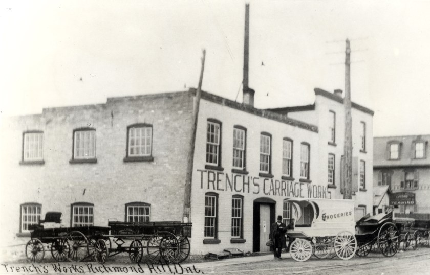 A photograph of Trench Carriage Works (ca. 1910) with a man standing out front beside a grocery wagon