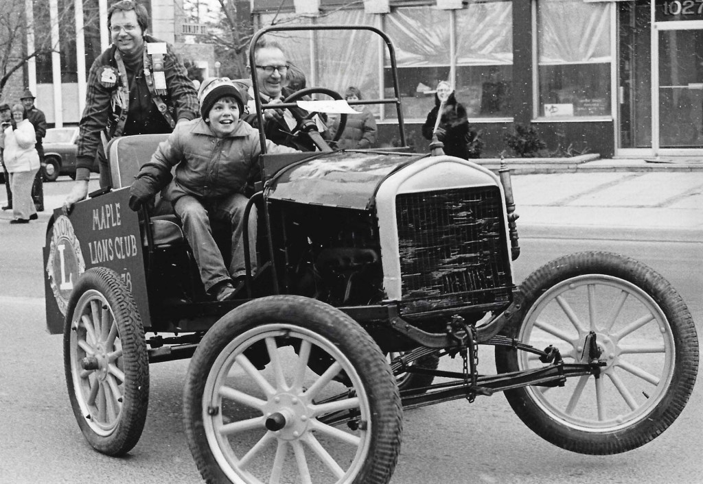 Black and white photograph of Frank Robson (driving), Bruce Murchison (Lion member) and Matt Smith (youth) in a parade in Richmond Hill.