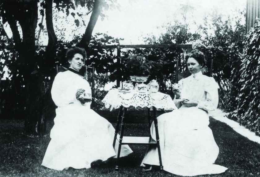 Black and white photograph from the early 1900s of Margaret McConaghy (left) and Effie (Hollingshead) Smith having tea in the garden, with lace tablecloth.